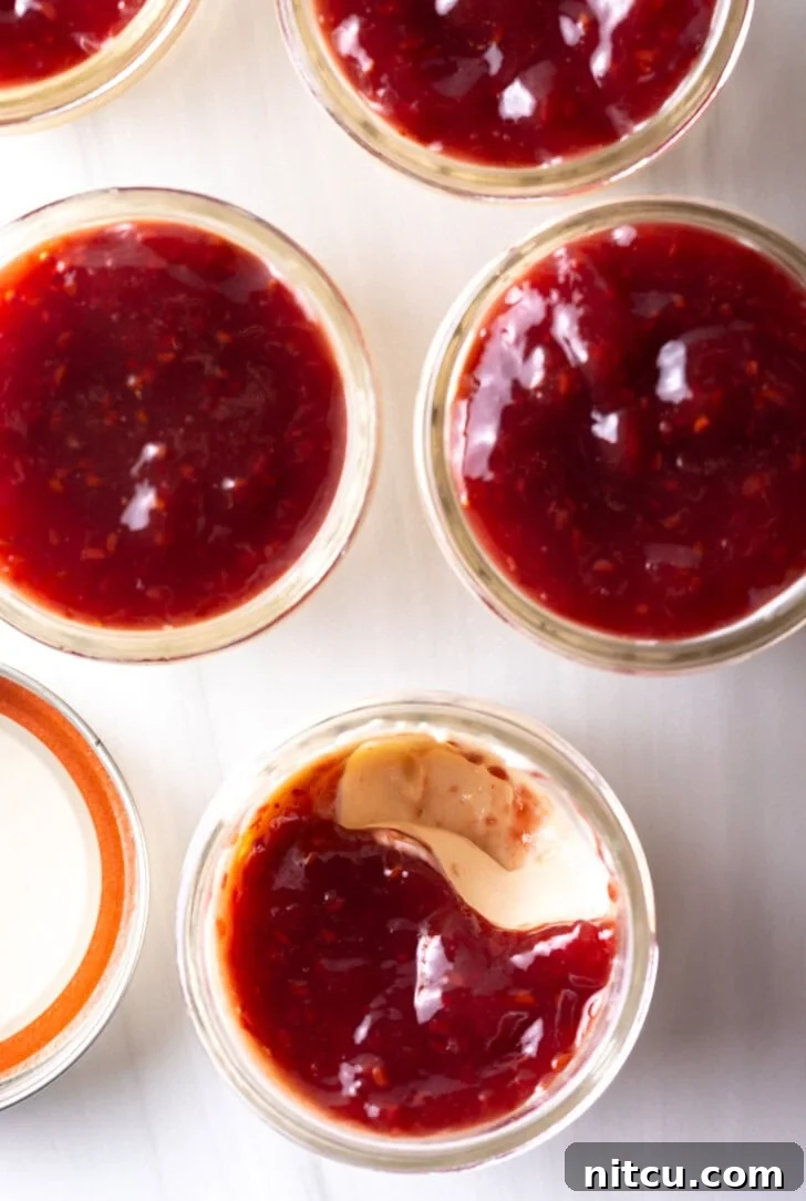 High-Protein Yogurt Pudding 3 Top down view of 4 glass jars of protein yogurt topped with raspberry jam.
