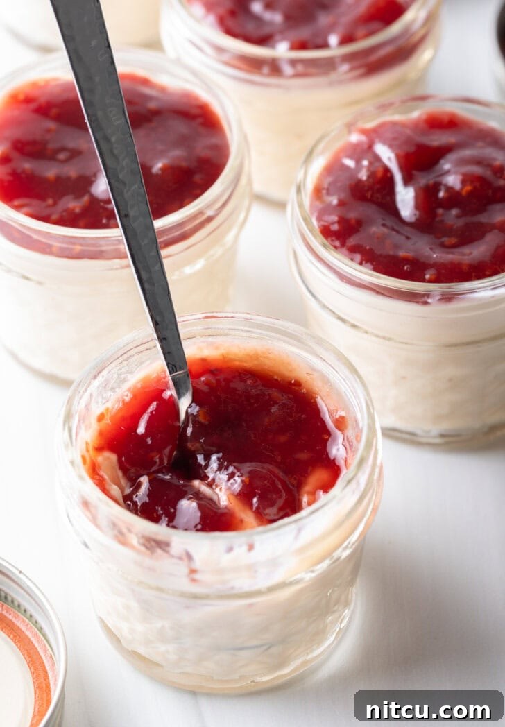 High-Protein Yogurt Pudding 4 Top down view 4 small glass jars of protein pudding topped with raspberry jam. A metal spoon is in the jar closest to camera.