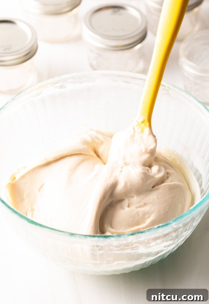 High-Protein Yogurt Pudding 6 Glass bowl with homemade protein yogurt being whipped with a yellow spatula.