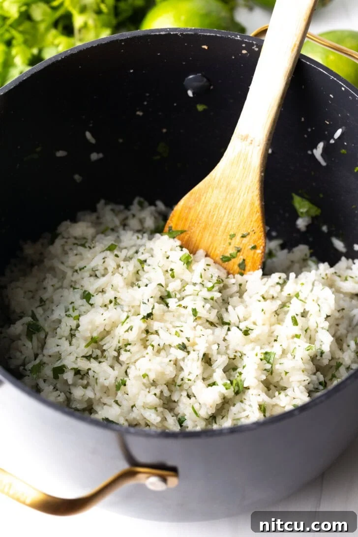 Homemade Chipotle Cilantro Lime Rice 9 Wooden spatula stirring fluffy white rice with chopped cilantro in a large cooking pot.