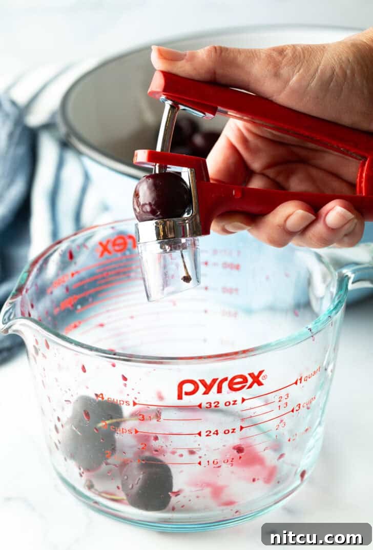 Sweet Cherry Pie Delight 6 A hand skillfully uses a cherry pitter to remove the pit from a fresh cherry, illustrating a key preparation step for a homemade cherry pie.