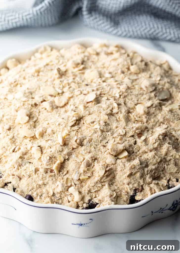 Perfect Blueberry Crisp 8 A baking dish filled with blueberries, covered generously with an uncooked, crumbly oat and almond topping, ready to be baked.