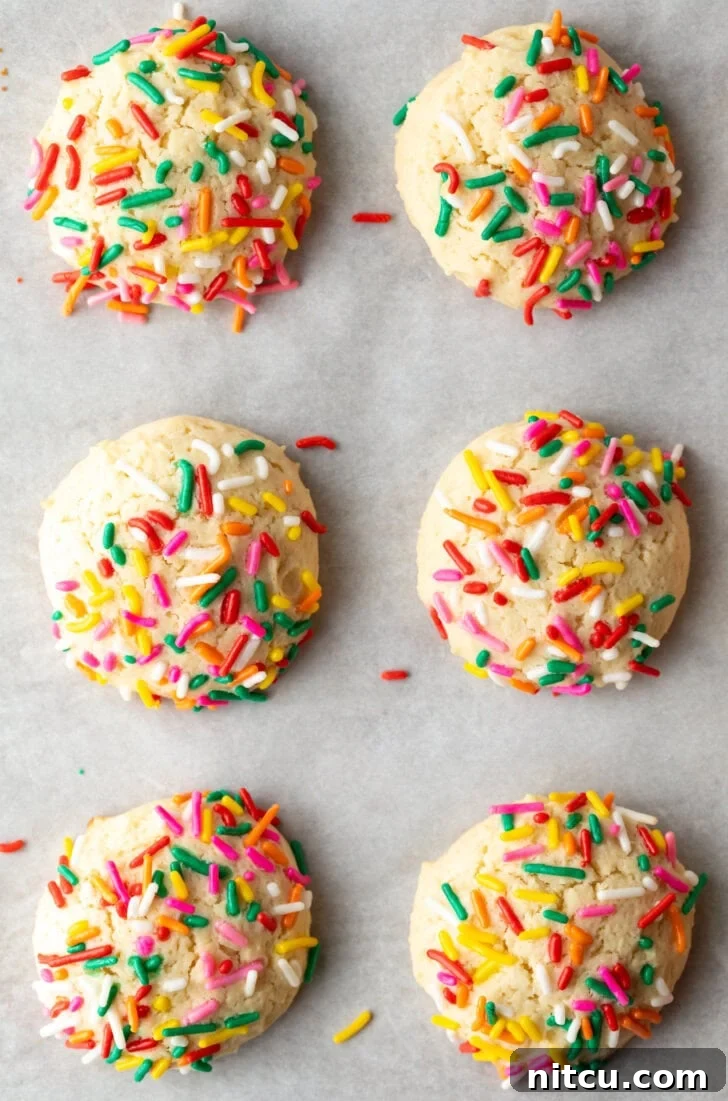 Velvety Cream Cheese Bites 3 Top down view 6 cream cheese cookies on a baking sheet, each topped with sprinkles.