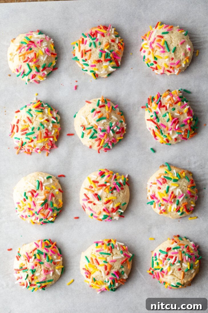 Velvety Cream Cheese Bites 7 Top down view 12 cream cheese cookies on a baking sheet, each topped with sprinkles.
