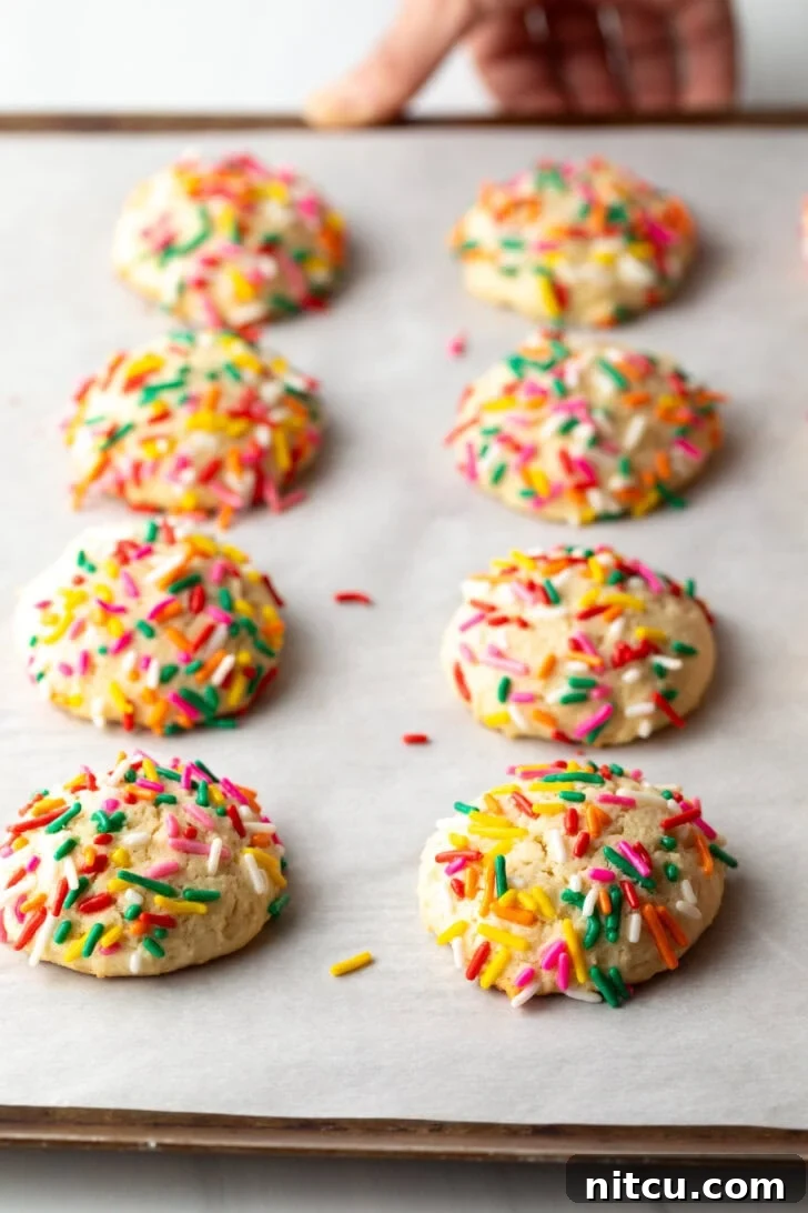 Velvety Cream Cheese Bites 8 8 cream cheese cookies on a baking sheet, each topped with sprinkles.