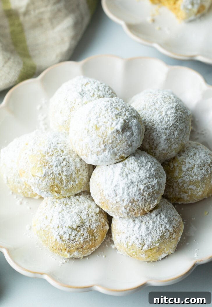 A beautiful pyramid stack of almond and pistachio Italian wedding cookies, each perfectly round and generously dusted with powdered sugar, ready for serving.