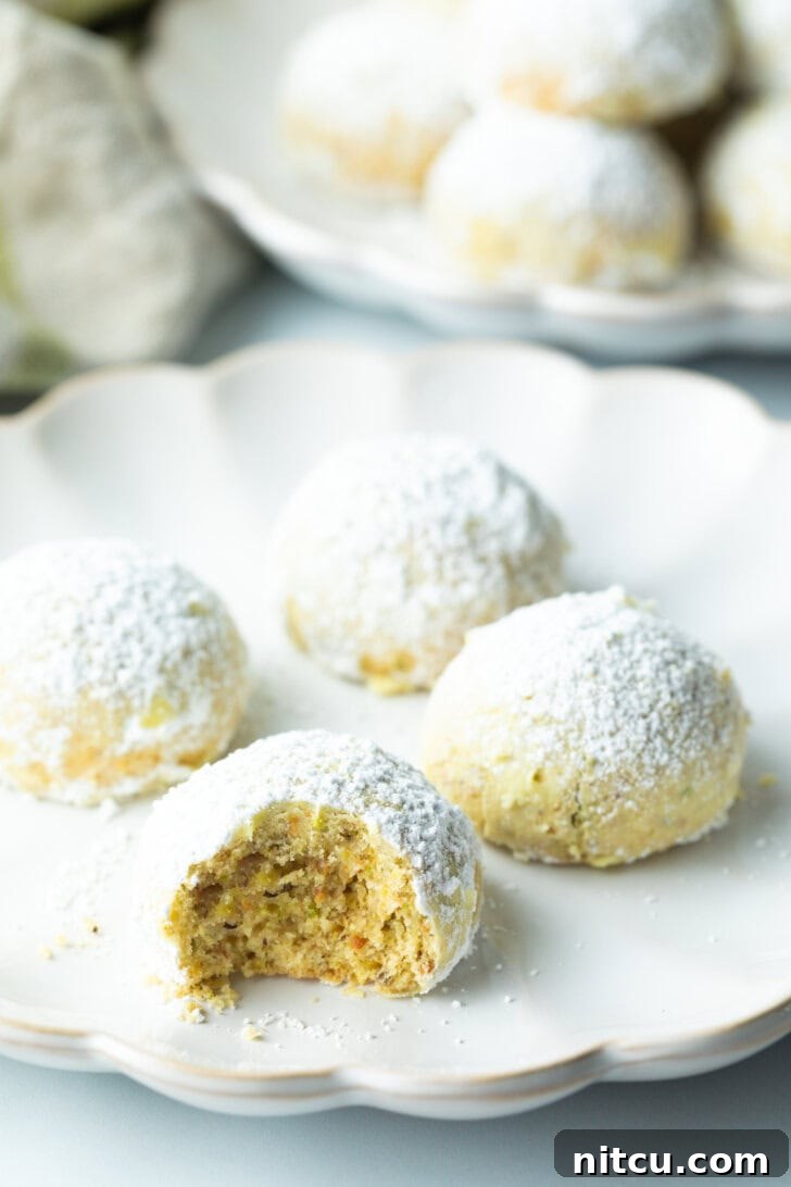 Another tempting view of four Italian wedding cookies, glistening with powdered sugar. The cookie closest to the camera has been bitten into, inviting a taste.