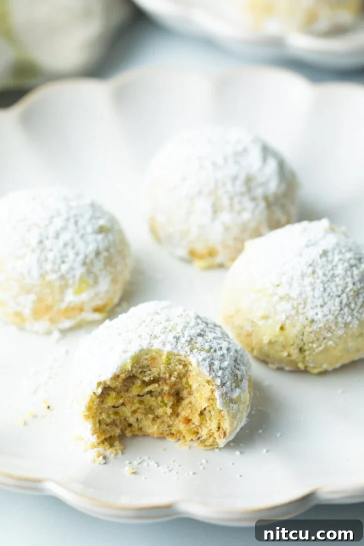 Close-up of four Italian wedding cookies, generously dusted with powdered sugar. The closest cookie has a tempting bite taken out, revealing its rich, nutty interior.