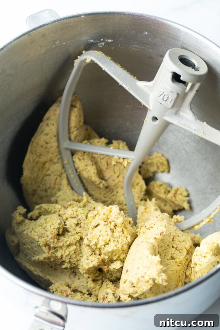 Cookie dough mixture in a metal mixing bowl, with the mixer paddle resting inside, ready for shaping.