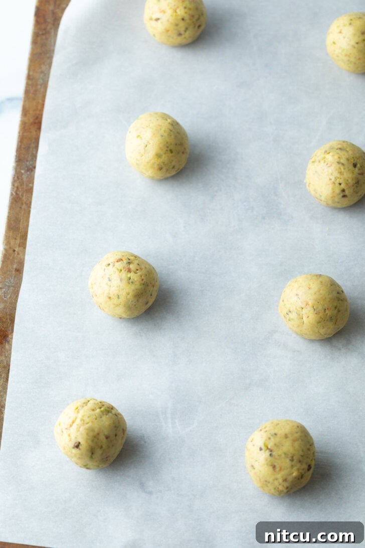 Eight perfectly portioned balls of cookie dough arranged neatly on a parchment-lined baking sheet, spaced for even baking.