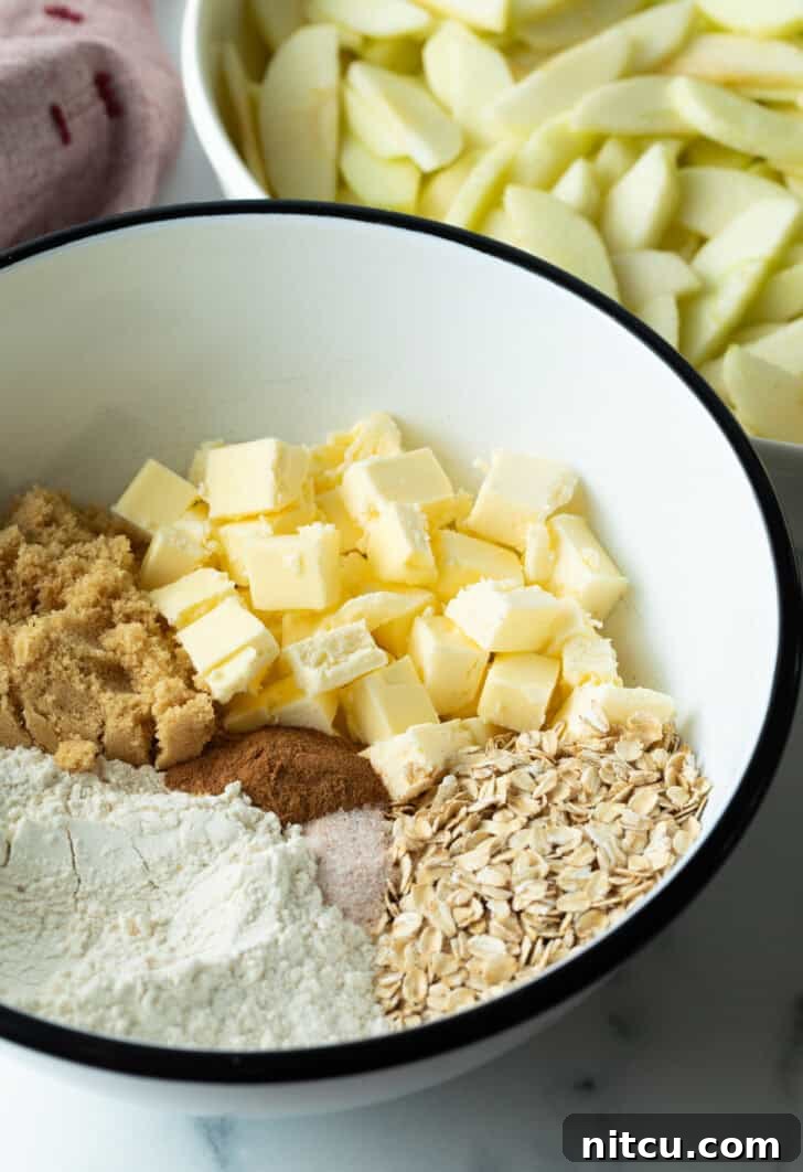 Effortless Golden Apple Crisp 5 White bowl with flour, cubes of butter, brown sugar, oats, and spices, ingredients for apple crisp topping.