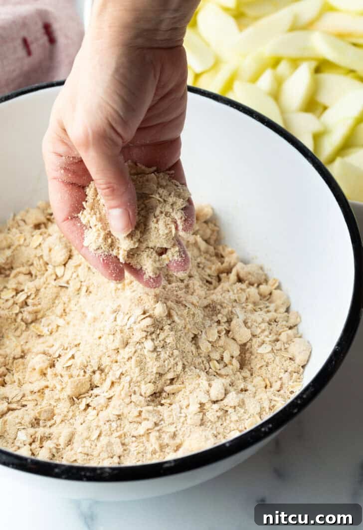 Effortless Golden Apple Crisp 6 Hand mixing oat crumbly topping in a white bowl, showing the texture of the crisp topping.