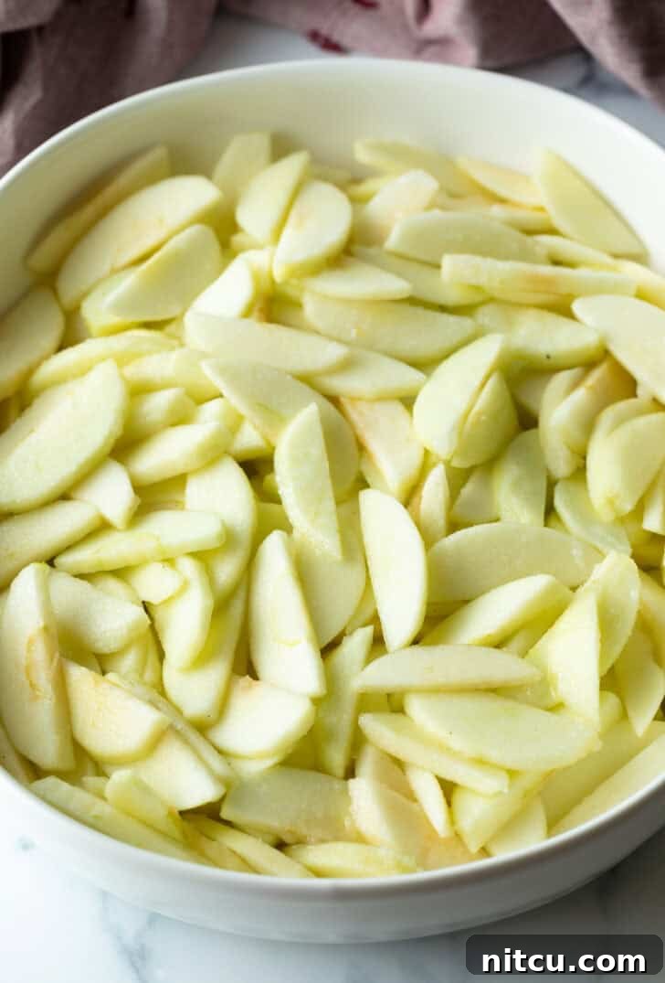 Effortless Golden Apple Crisp 7 White oval baking dish filled with thinly sliced apples, prepared for apple crisp filling.