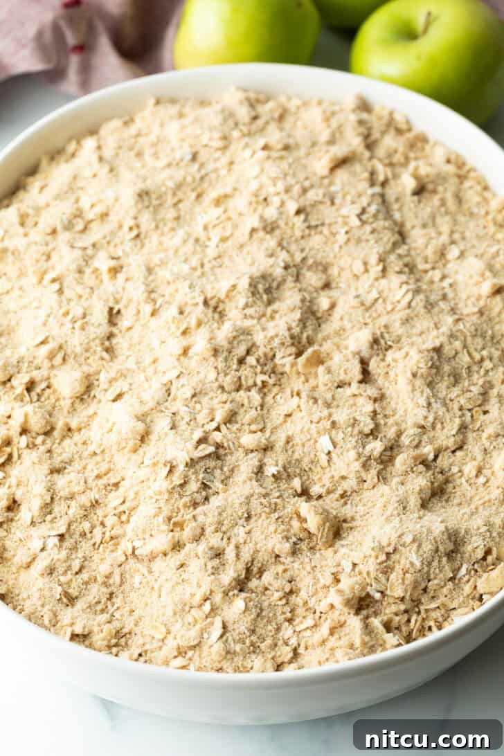 Effortless Golden Apple Crisp 8 Raw oat crumble topping spread evenly over apple slices, ready for baking.
