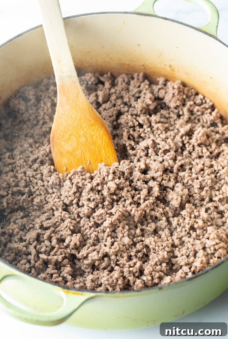 Ground venison meat browning in a large cooking pot, being stirred with a wooden spatula.