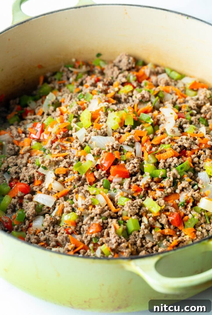 Cooking ground deer meat with a medley of chopped vegetables in a spacious pot, enhancing flavor and texture.