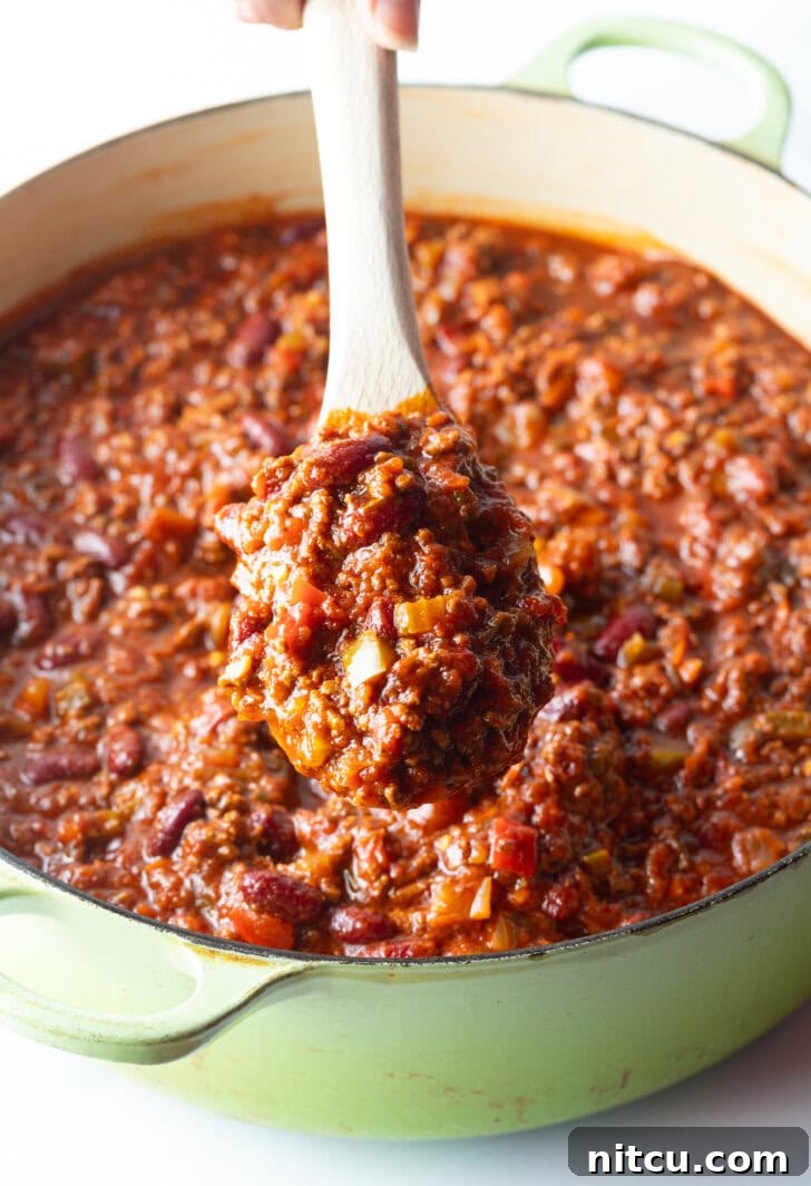 A close-up view of a wooden spoon lifting a hearty scoop of meaty deer chili, showcasing its rich texture and steam.