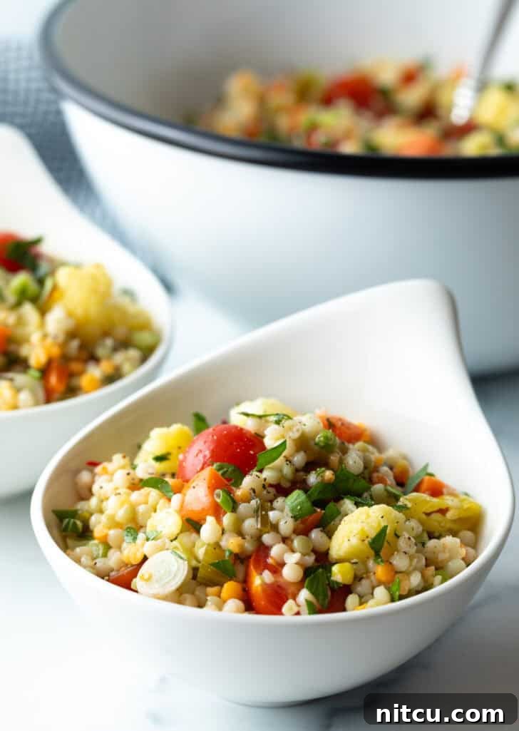 A vibrant serving of Israeli couscous salad in a white bowl, ready to be enjoyed.