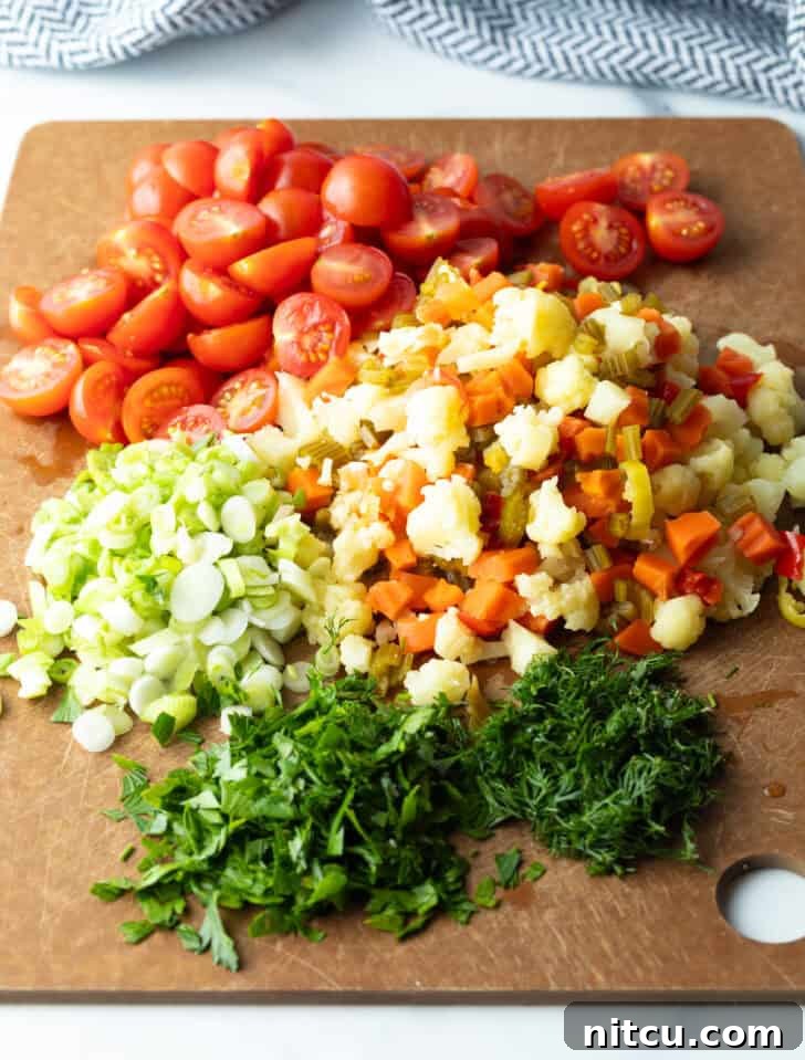 Chopped cherry tomatoes, scallions, parsley, and pickled vegetables neatly arranged in piles on a brown cutting board, prepped for the salad.