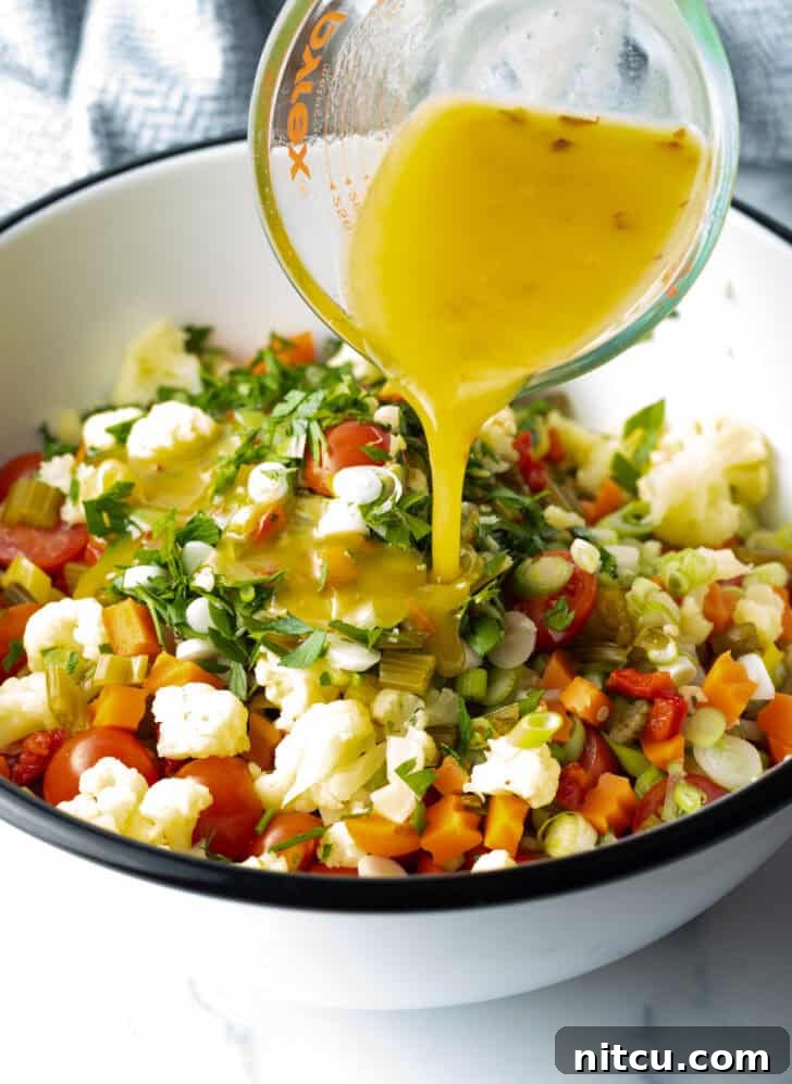 Pouring the tangy Giardiniera vinaigrette over the colorful medley of veggies and couscous in a large mixing bowl.