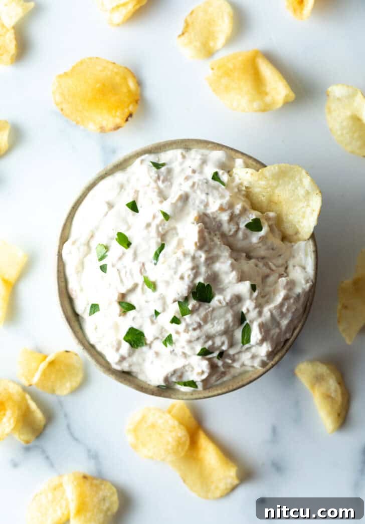 A vibrant top-down view of the French onion dip, adorned with a sprinkle of fresh chives and a crisp potato chip ready for scooping.