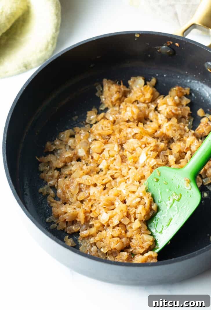 Finely diced onions gently caramelizing in a large skillet, stirred with a green spatula, slowly turning golden brown.