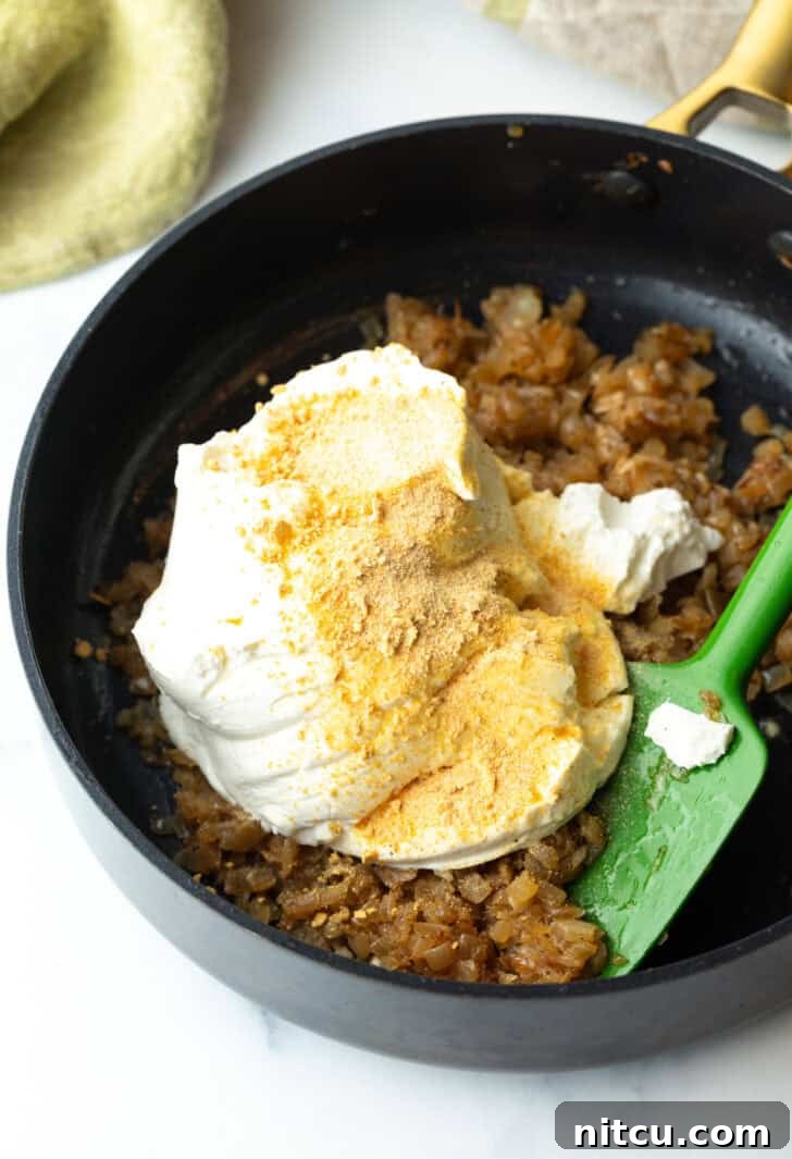 Cooked and cooled caramelized onions are placed in a large mixing bowl, ready to be combined with sour cream, mayonnaise, and a blend of savory spices.