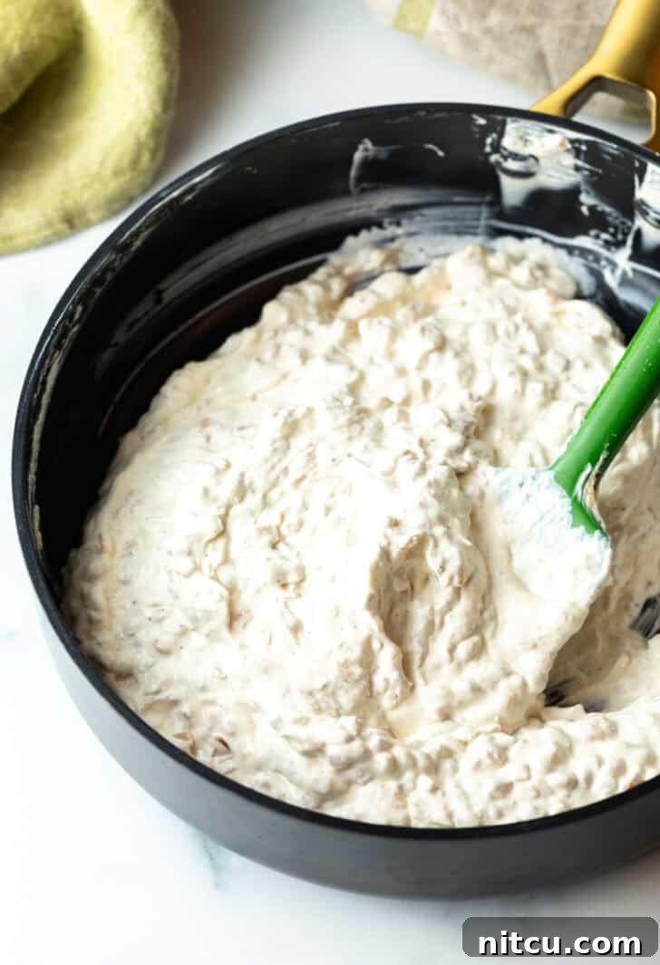 The creamy dip being thoroughly stirred in a large bowl with a green spatula, ensuring all ingredients are well incorporated and the flavors meld.