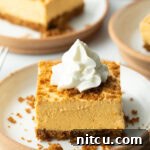 Sheet Pan No-Bake Pumpkin Cheesecake 14 Square of pumpkin pie cheesecake on a white plate, topped with whipped cream.