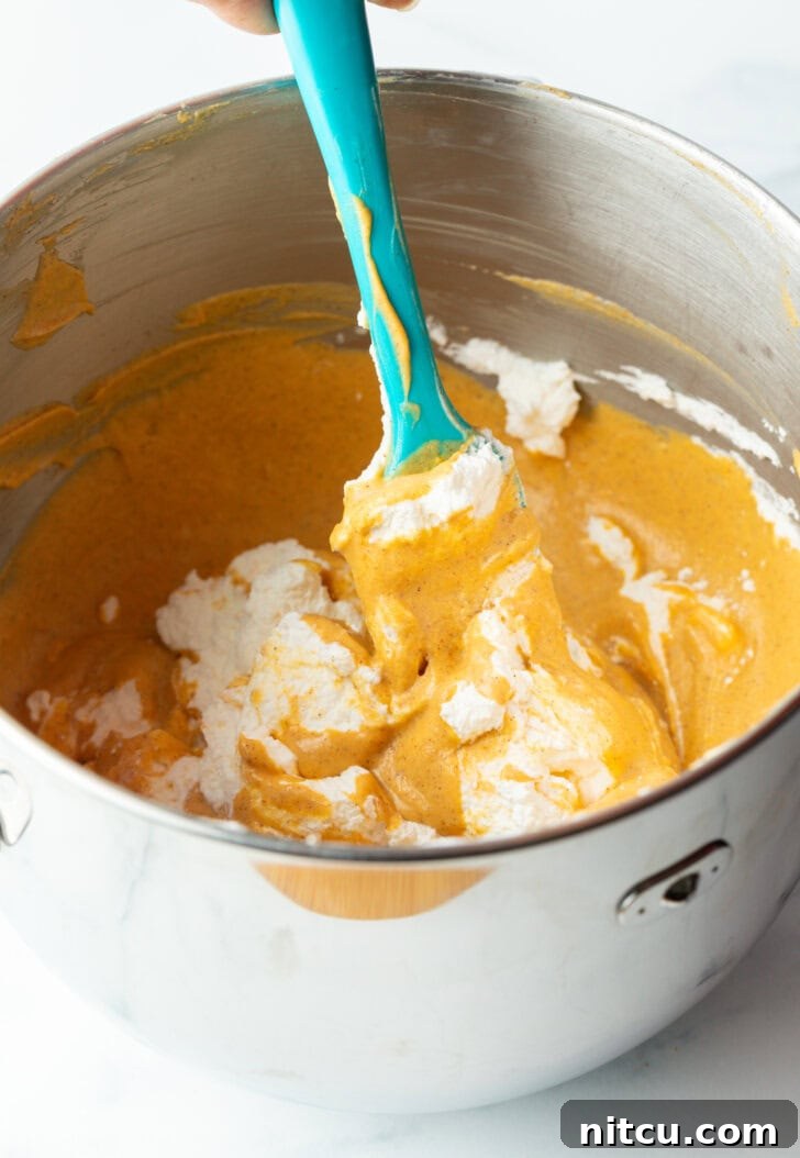 Sheet Pan No-Bake Pumpkin Cheesecake 8 Pumpkin puree and cream cheese being mixed together with a blue spatula in a large metal bowl.