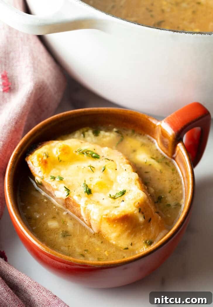 Bistro Onion Comfort 11 Large red mug with French onion soup, topped with a slice of baguette with melted cheese, ready to be served.