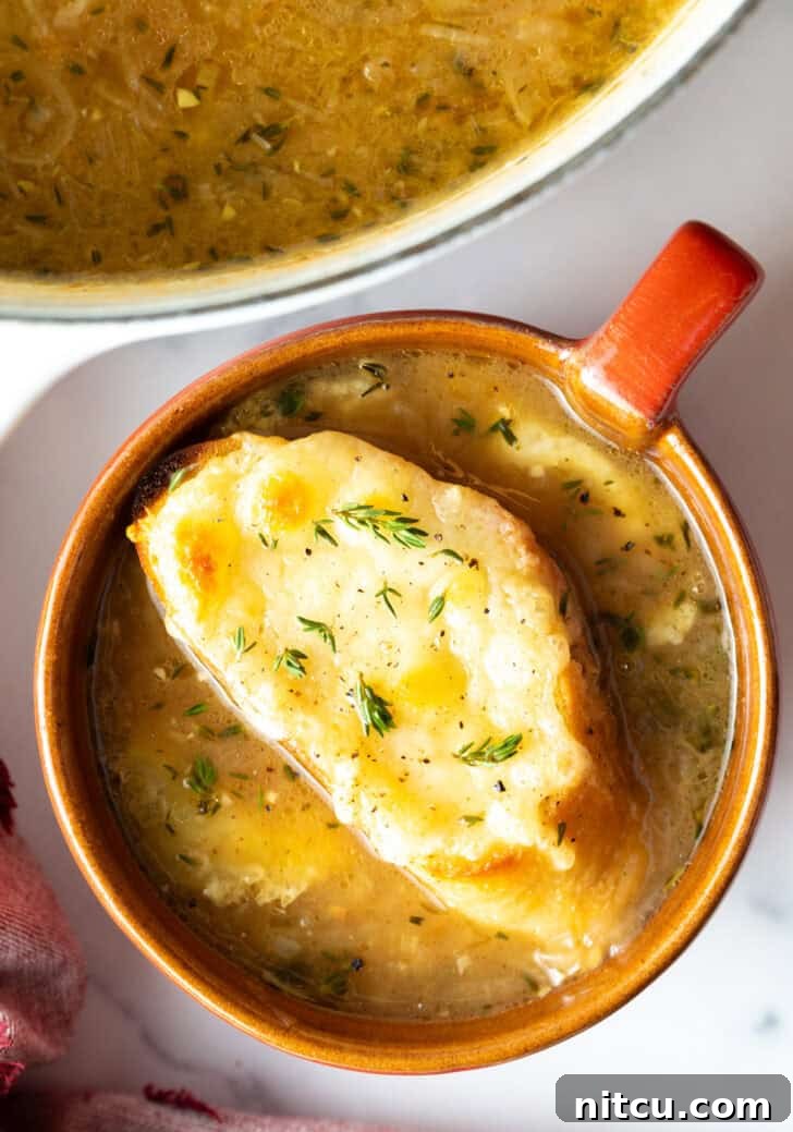 Bistro Onion Comfort 4 Top down view of a large red mug with French onion soup, topped with a slice of baguette with melted cheese.