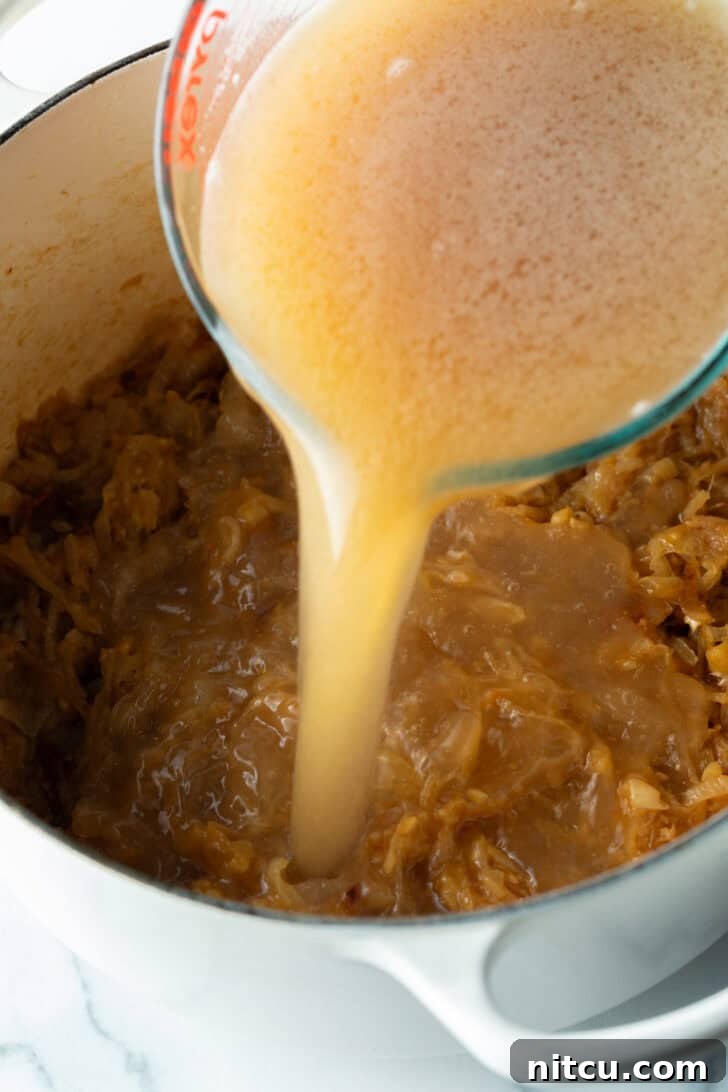 Bistro Onion Comfort 7 Pouring beef stock from a glass pitcher into the large pot with cooked onions.