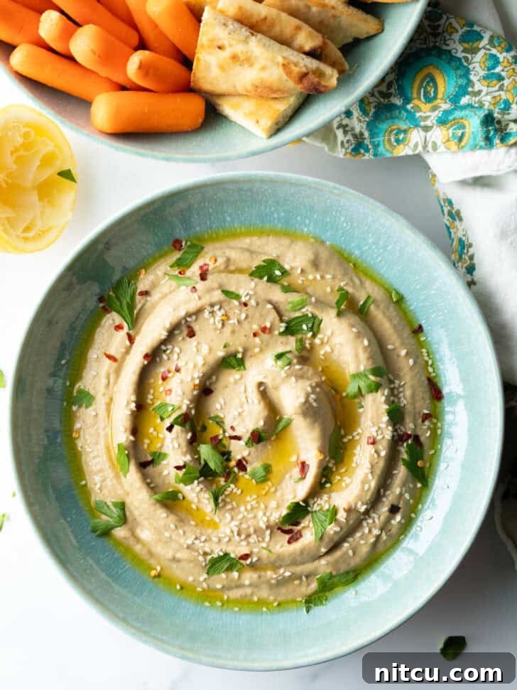 Top-down view of a light blue bowl of baba ganoush, artfully garnished with a swirl of olive oil and a few parsley sprigs.