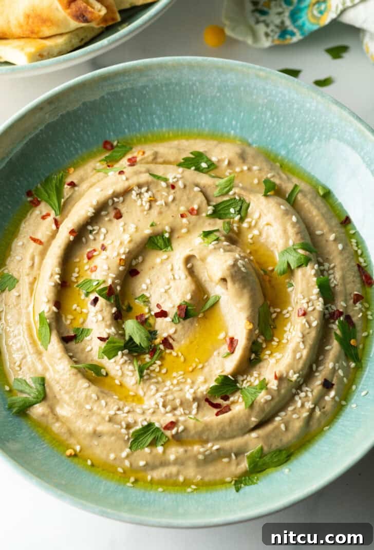 Top-down view of a light blue bowl filled with smooth baba ganoush, garnished with a swirl of olive oil and a sprinkle of paprika.
