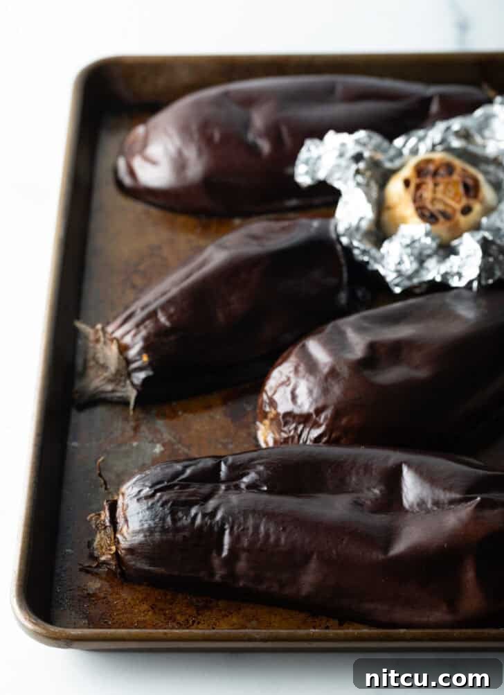 Roasted eggplant halves on a baking sheet, their flesh browned and softened.