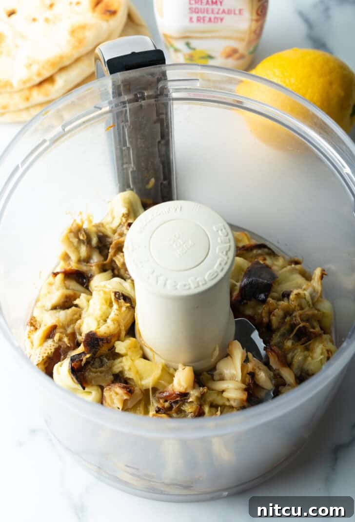 Chopped roasted garlic cloves and scooped eggplant flesh in a food processor, ready to be blended.