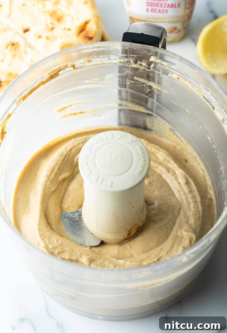 Smooth, pureed eggplant dip swirling in a food processor, indicating a creamy consistency.