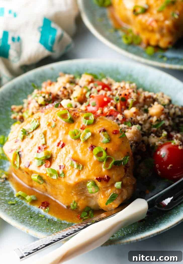 Tender Baked Pork Chops 2 A perfectly baked pork chop, richly coated in a glistening savory-sweet glaze and garnished with fresh chopped scallions, presented on a white plate alongside a vibrant quinoa salad with cherry tomatoes.