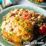Baked pork chop covered with glaze and chopped scallions, on a plate next to quinoa salad with tomatoes.