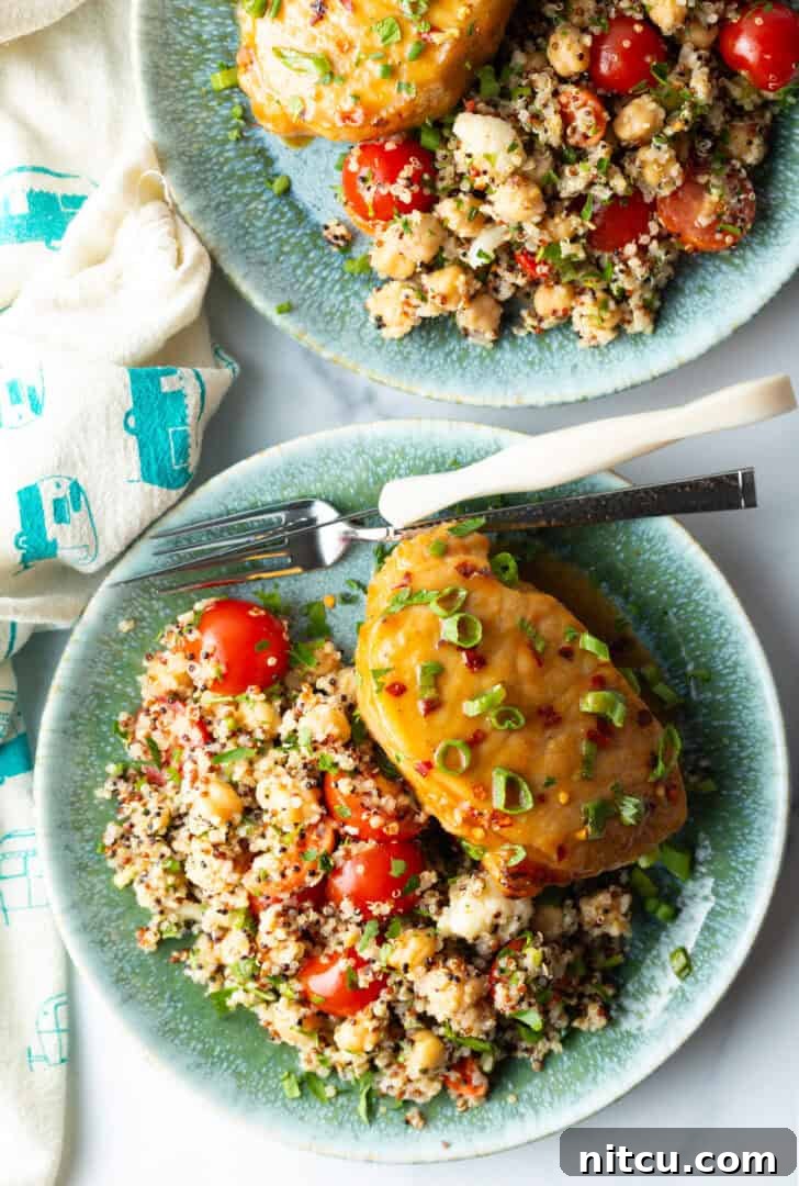 Tender Baked Pork Chops 4 A perfectly cooked baked pork chop, gleaming with its savory-sweet glaze and adorned with fresh chopped scallions, elegantly plated beside a wholesome quinoa salad featuring vibrant tomatoes.