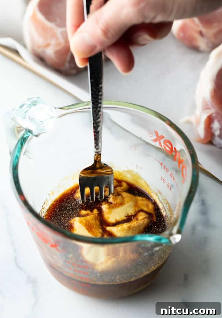 Tender Baked Pork Chops 5 A close-up of a fork stirring together light brown sugar, soy sauce, and Dijon mustard, along with garlic powder, in a clear glass measuring cup, showcasing the beginnings of the rich glaze.