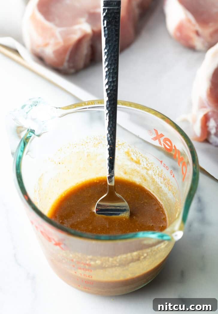 Tender Baked Pork Chops 6 The perfectly emulsified brown soy and Dijon glaze ingredients resting in a glass measuring cup with a fork, exhibiting a smooth, inviting consistency ready for application.