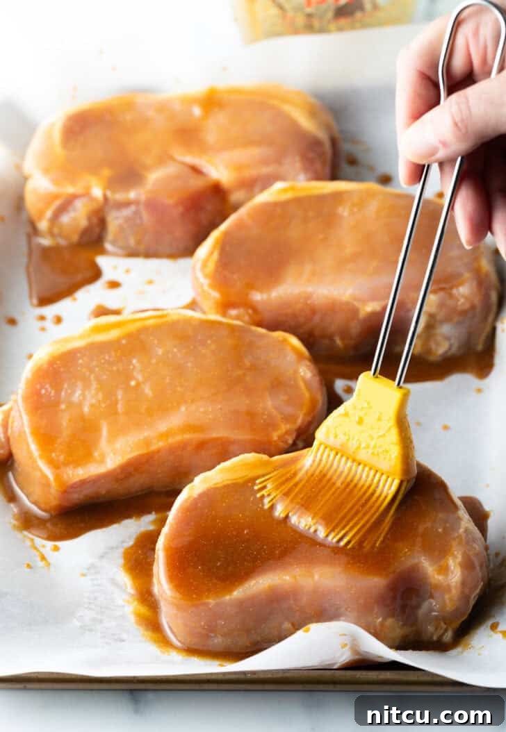 Tender Baked Pork Chops 7 A chef's brush carefully applying the rich, savory-sweet glaze over raw pork chops arranged on a baking sheet, ensuring full coverage before baking.