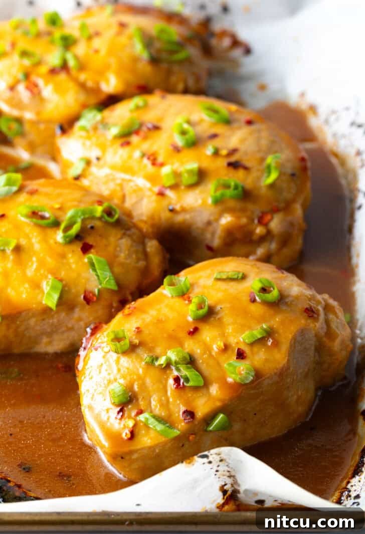 Tender Baked Pork Chops 9 Beautifully glazed pork chops, freshly baked and generously covered with bright green onions, resting on a baking sheet, emanating a delicious aroma and ready for serving.