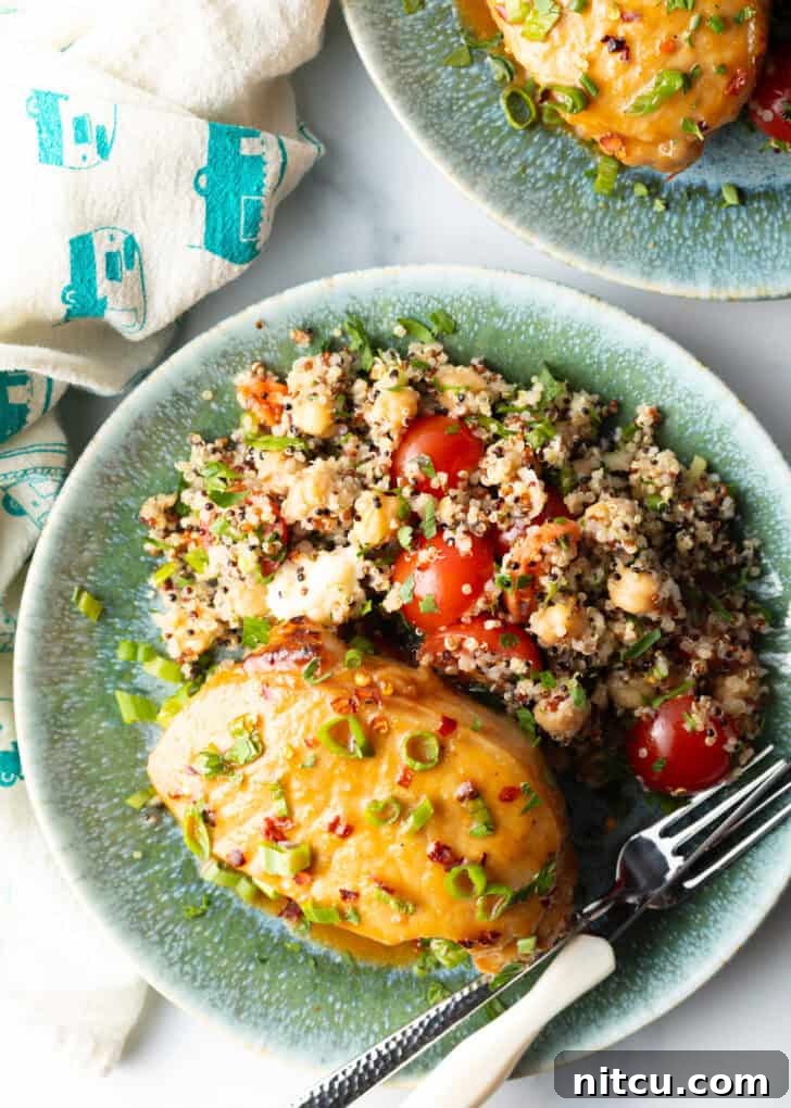 Tender Baked Pork Chops 10 A perfectly baked pork chop, covered with a shiny glaze and fresh scallions, elegantly plated beside a wholesome quinoa salad with bright red tomatoes, presenting a complete and inviting meal.