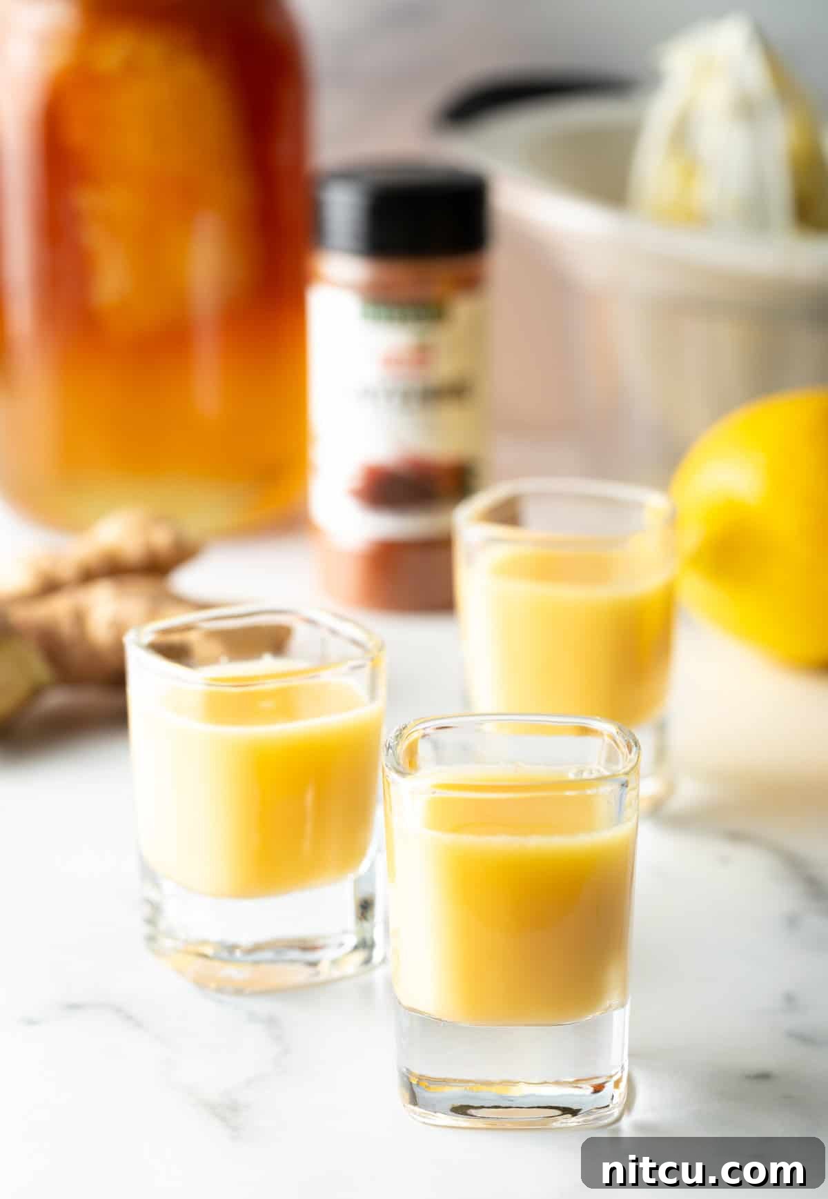 Ginger Zinger Immunity Elixir 7 Three shot glasses with golden yellow ginger shots, garnished with lemon slices, ready for serving.