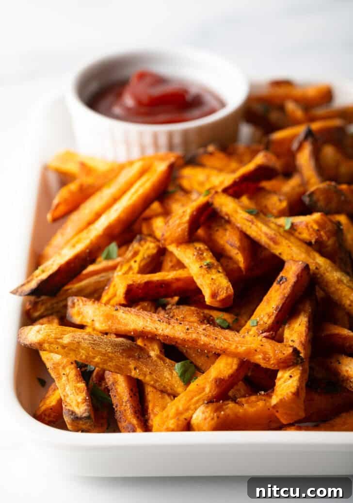 Crispy Air Fryer Sweet Potato Fries 2 Piles of cooked sweet potatoes on a large serving pan with a white ramekin of ketchup.
