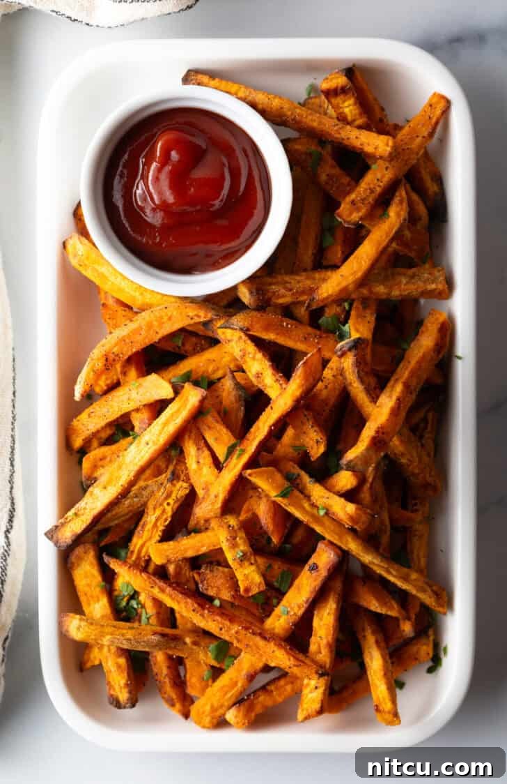 Crispy Air Fryer Sweet Potato Fries 11 Piles of cooked air fryer sweet potatoes on a large serving pan with a white ramekin of ketchup.