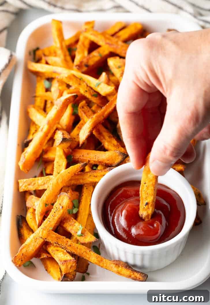 Crispy Air Fryer Sweet Potato Fries 12 Hand dipping a sweet potato fry from air fryer in a white ramekin of ketchup.